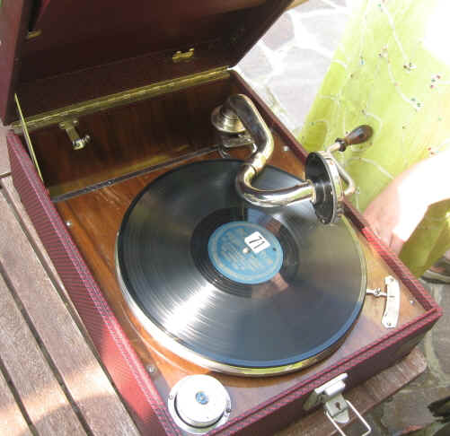 Geöffnetes tragbares Grammophon mit aufgelegter Schallplatte und sichtbarer Kurbel
