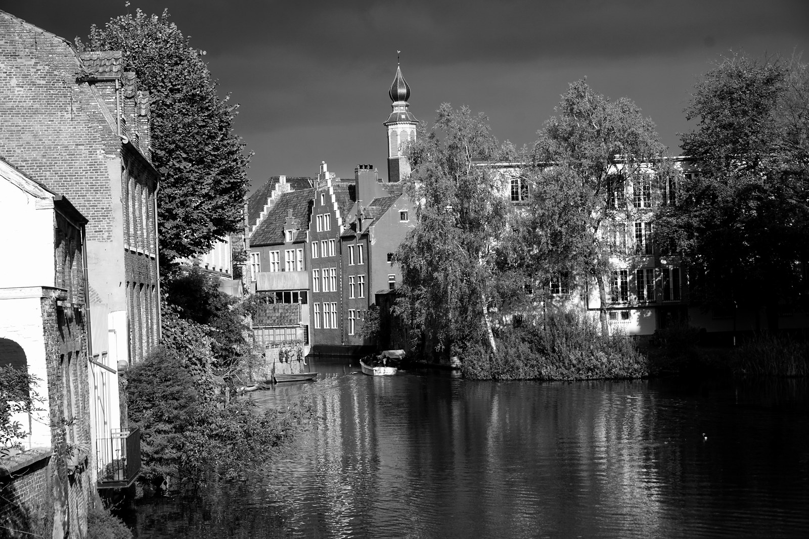 Schwarzweißfotografie eines stillen Genter Gewässers mit historischen Häusern und Bäumen