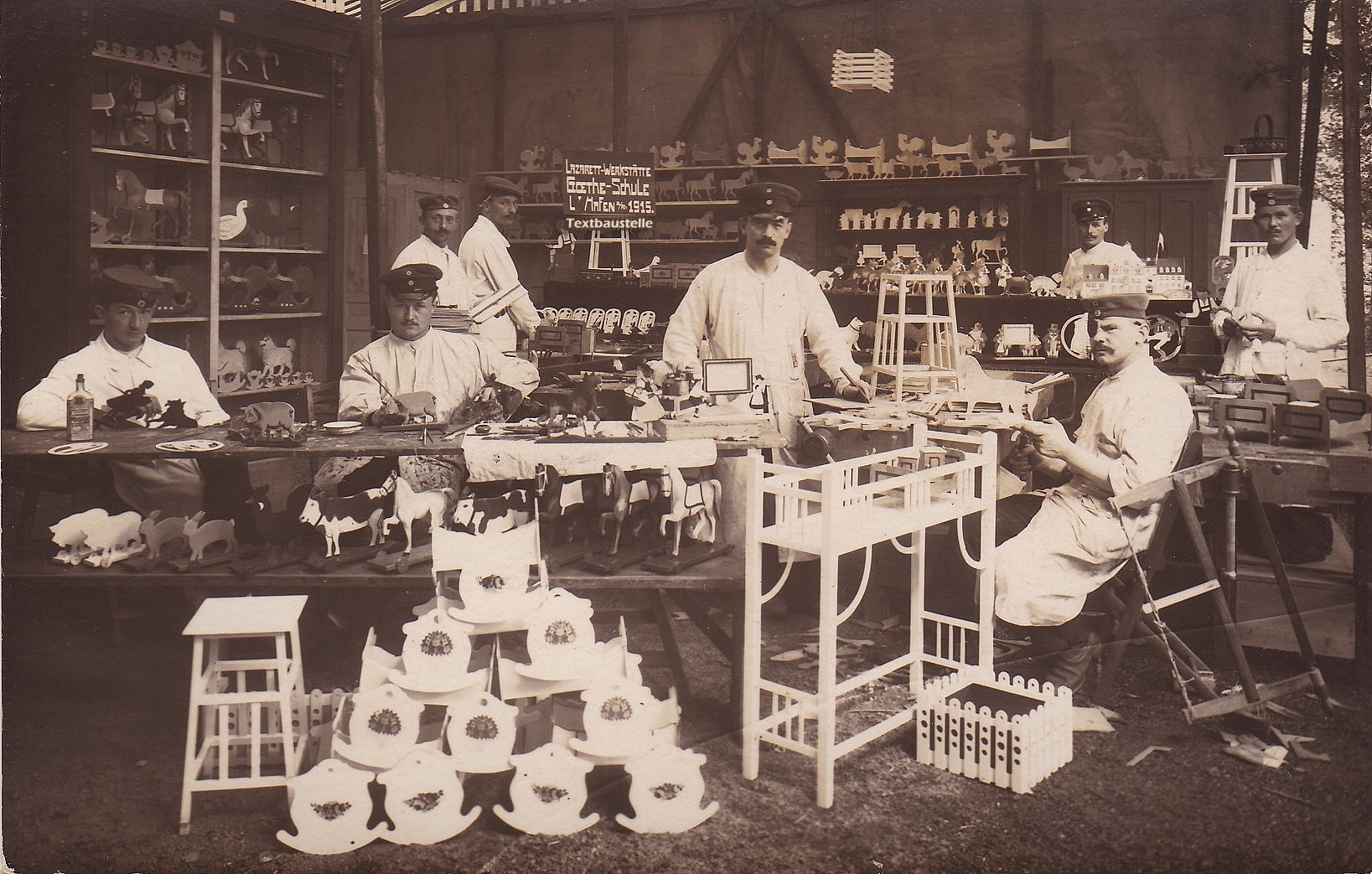 Historische Fotografie einer Lazarett-Werkstätte mit acht Männern zwischen hölzernen Tieren, Spielzeug und Arbeitsgeräten